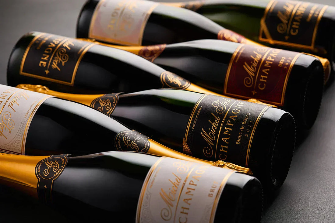 Lineup of a collection of Michel Foch Champagne bottles with elegant gold trim labels