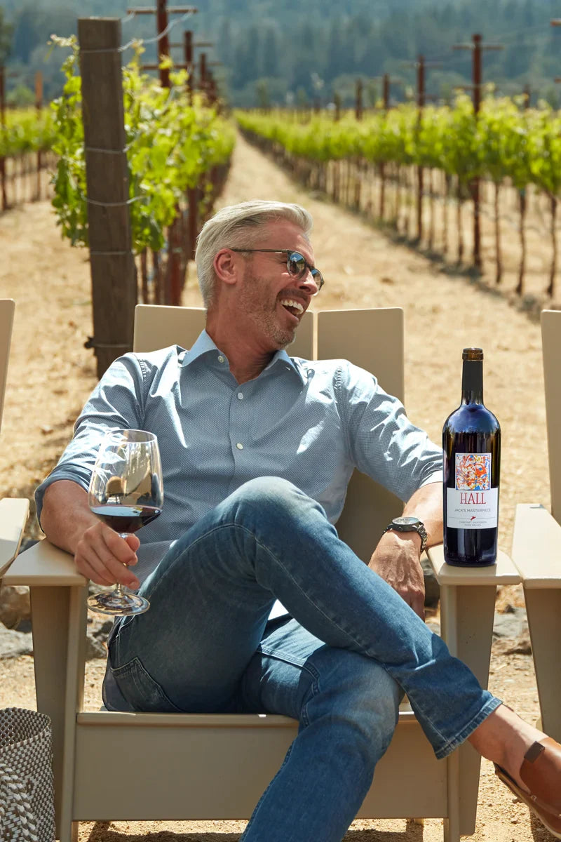 Man sitting in a vineyard with a bottle of Hall wine and a glass.