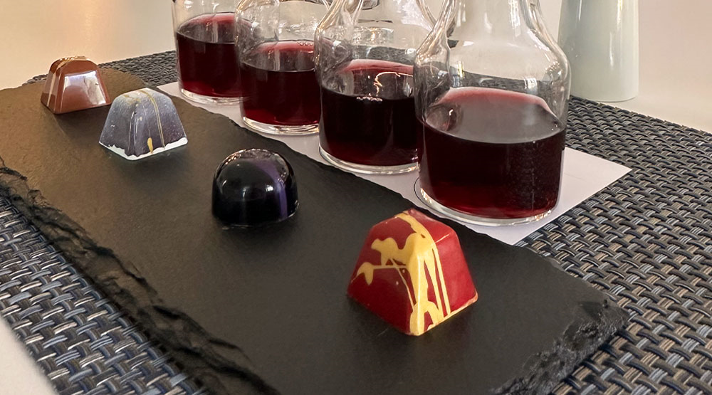 Hand crafted artisan chocolate on a stone serving slab in front of WALT Pinot Noir in tasting carafes. 