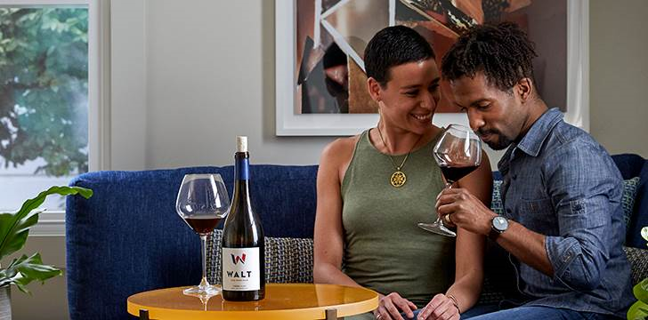 Couple enjoying WALT Pinot Noir together in a cozy setting at the WALT/BACA Healdsurg tasting room. 