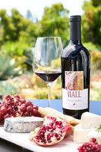 Bottle of 2022 HALL Terra Secca Cabernet Sauvignon on a table with a glass of red wine and a cheese platter in the foreground