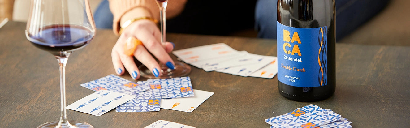 Person playing cards at a table with a bottle of Baca wine and a glass.