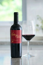 Image of a bottle of Kathryn Hall Napa Valley Cabernet Sauvignon nest to a glass of red wine displayed on a granite counter.