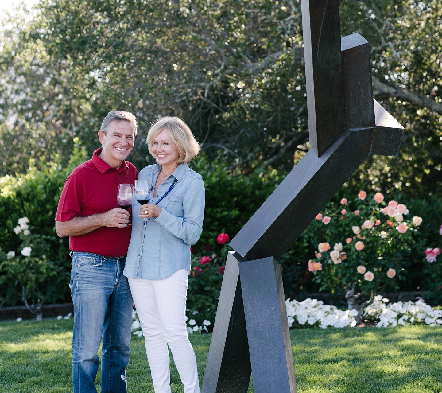 Man and woman standing in a garden with a modern sculpture and flowers in the background
