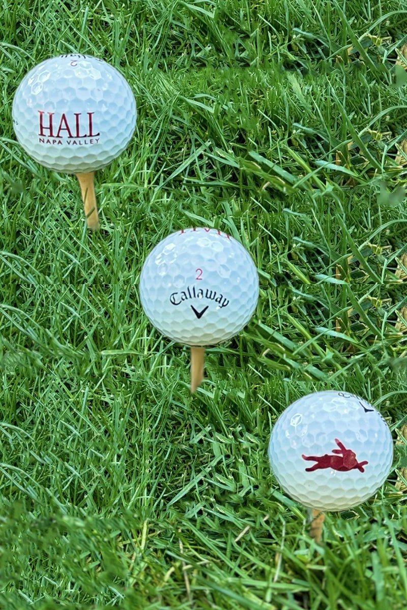 Three Callaway Chrome Tour golf balls featuring HALL Napa Valley and Bunny Foo Foo logos on tees in grass.