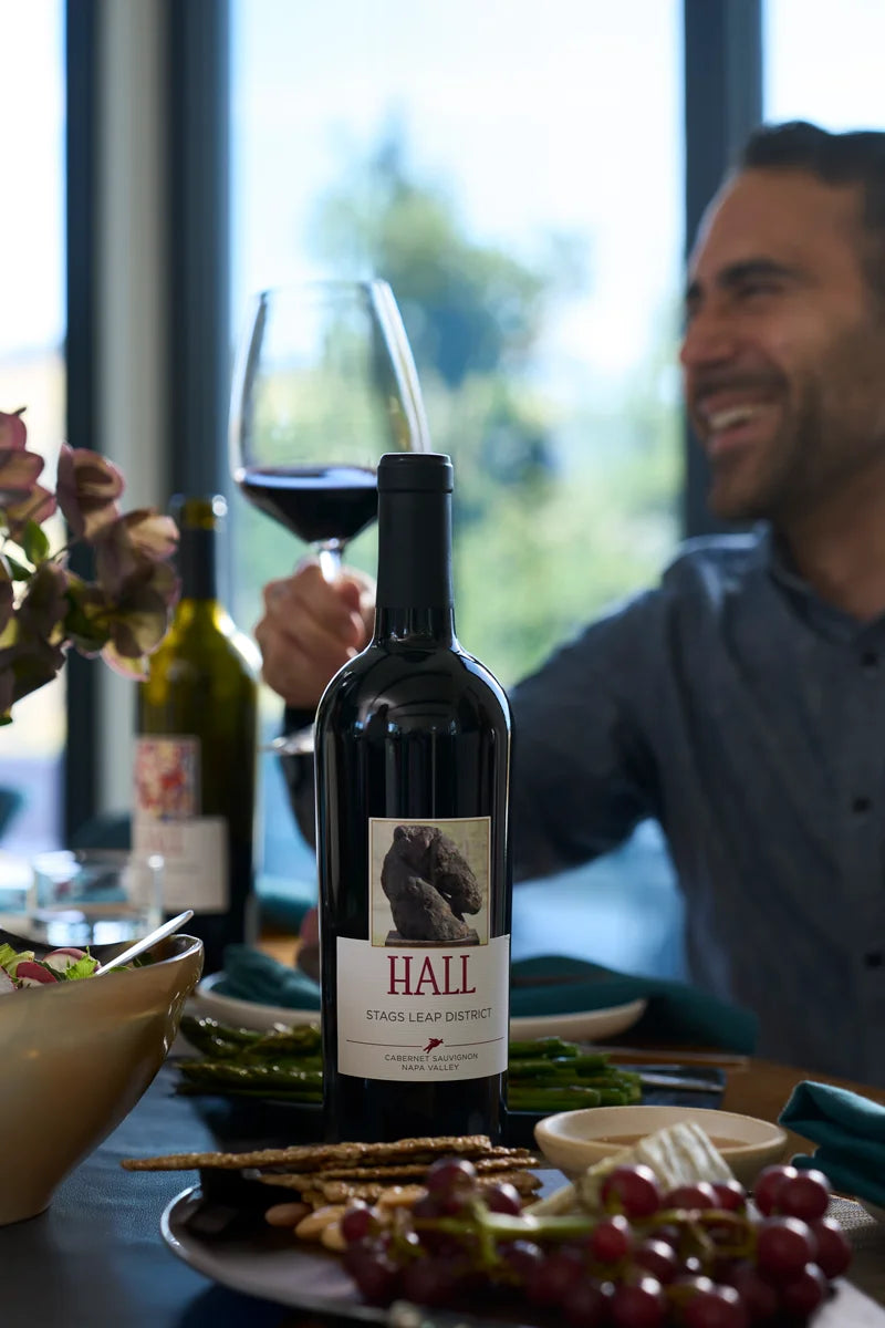 Person sitting at a table with a bottle of Hall wine, a glass, and food.