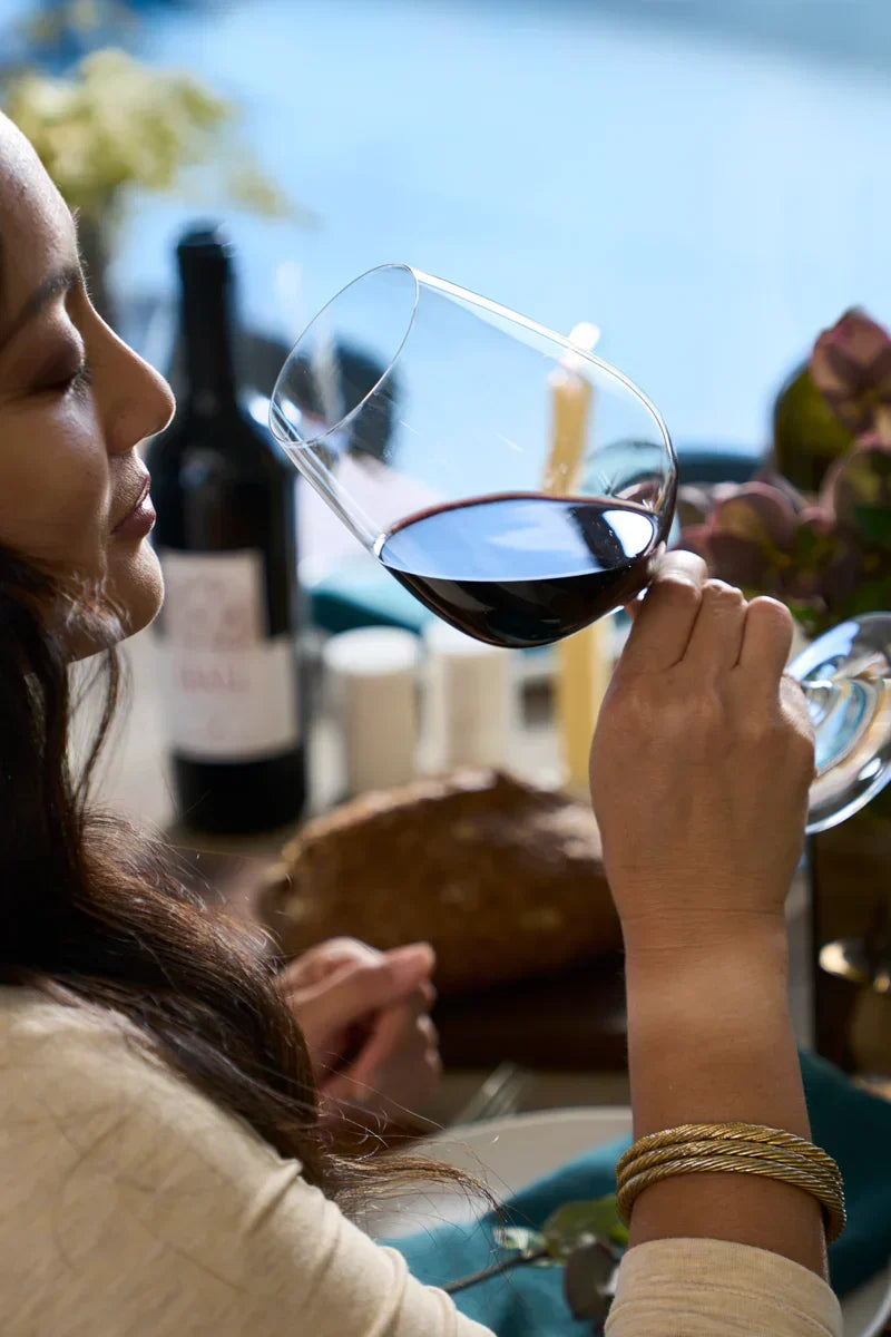 Woman savoring a glass of red wine at an outdoor dining table with food, with a slightly blurred bottle of HALL Bergfeld Cabernet Sauvignon in the background