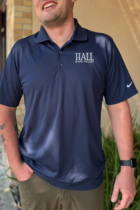 A photo of a man wearing a blue Nike golf polo with a White HALL Napa Valley logo embroidered on the right side of the chest.