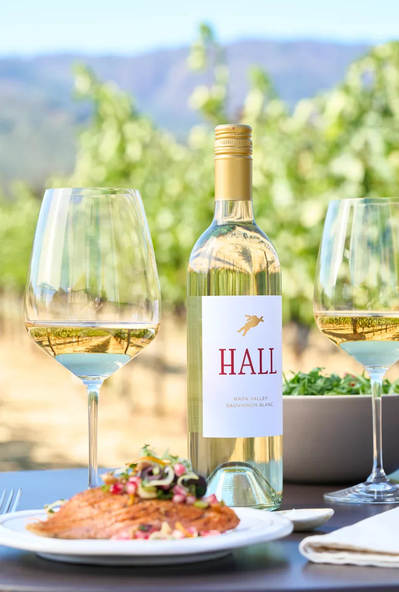 Bottle of HALL Napa Valley Sauvignon Blanc between two wine glasses containing white wine with a salmon dish in front.