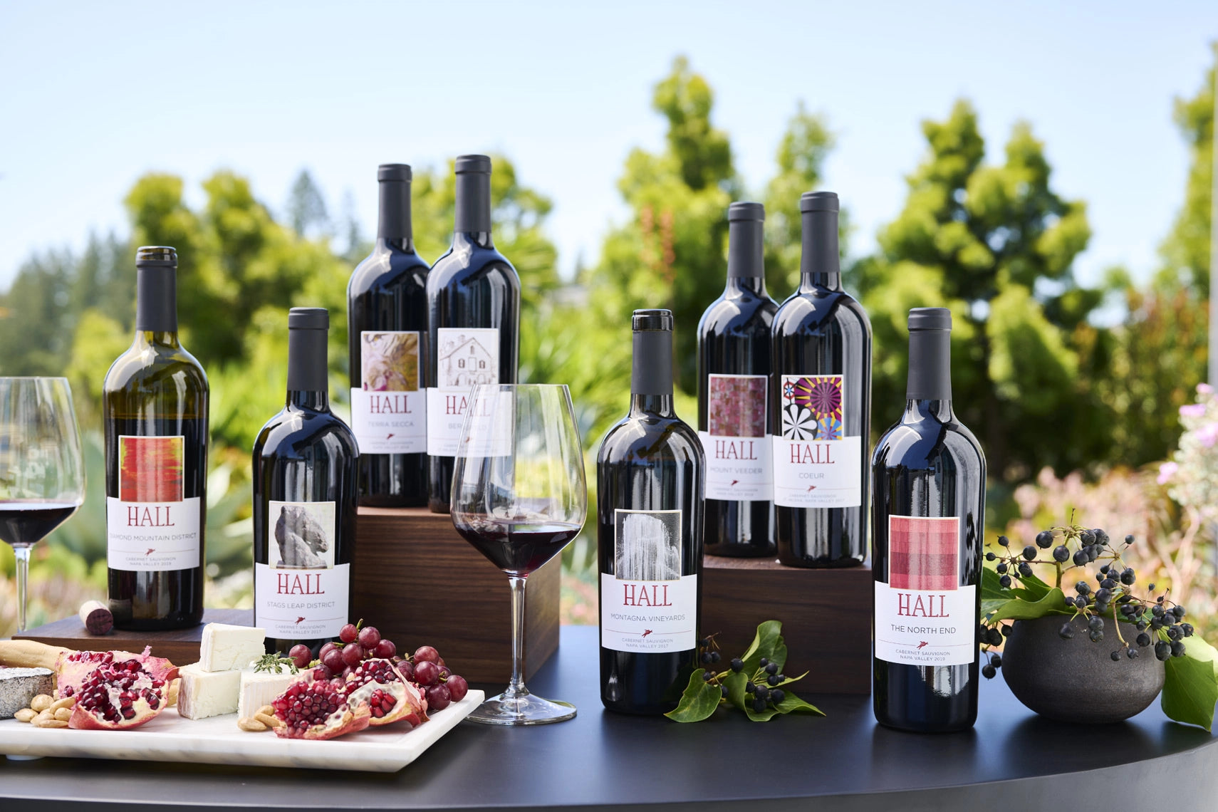 Collection of Hall wine bottles with glasses and snacks on a table outdoors.