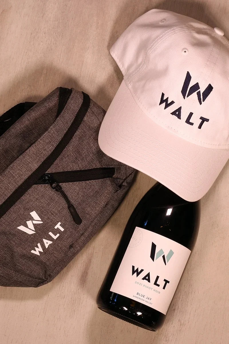 Image featuring the WALT New Era baseball cap, walt cross body bag and a bottle of WALT Blue Jay Pinot Noir.