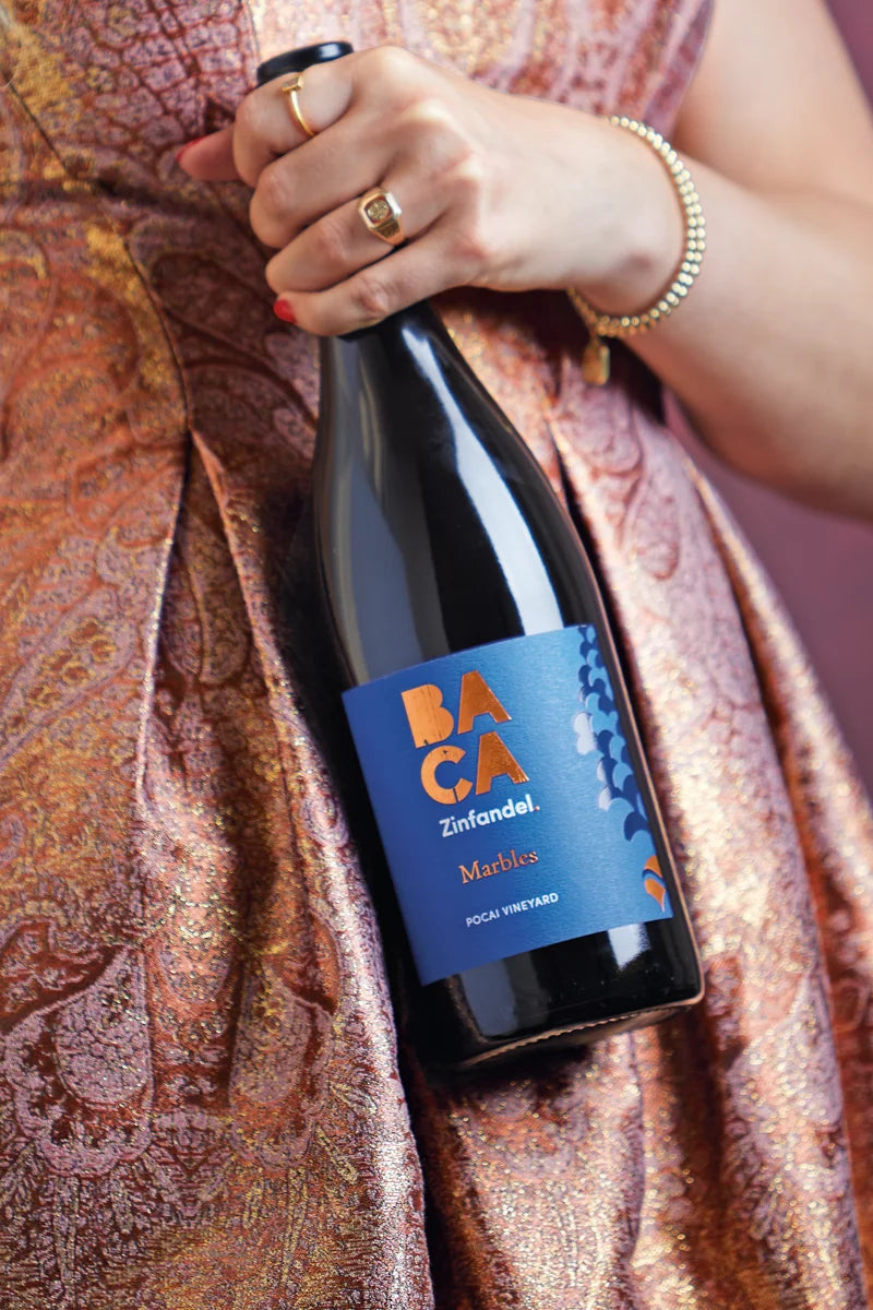 Person holding a bottle of Baca Zinfandel wine with a patterned fabric background