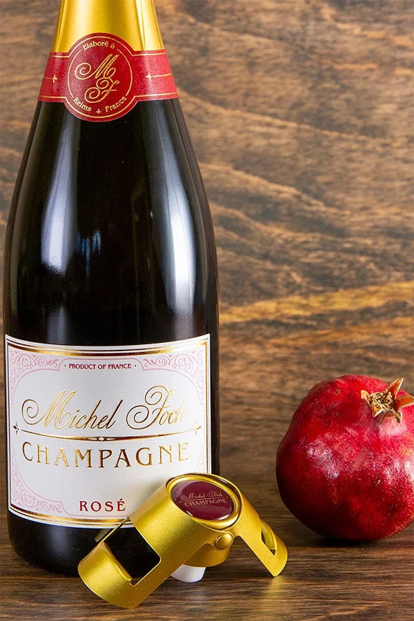 Image of a bottle of Michel Foch Rose Champagne, a gold bouchon branded with the Michel Foch Champagne logo and a pomegranate.