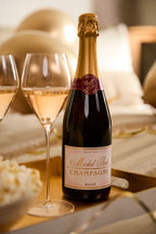 Festive scene with a bottle of Michel Foch Champagne Rosé and two glasses of sparkling rosé wine on a gold tray, gold balloons in the background, and a bowl of popcorn partially visible on the left.