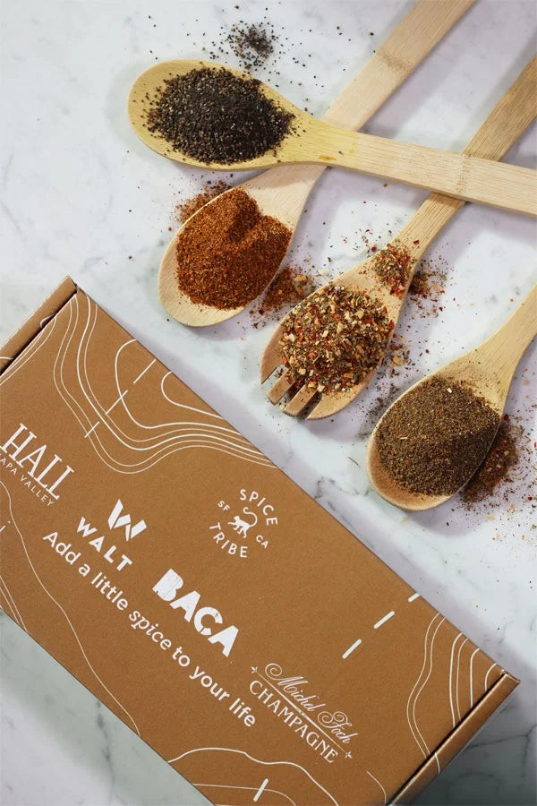 The HALL Family Spice Box displayed next to wooden spoons with the spices in the spoon on a white marble counter.