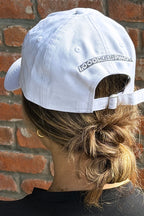 Image of a person wearing a New Era white cap with the WALT Wines 1000 Miles of Pinot on the back.